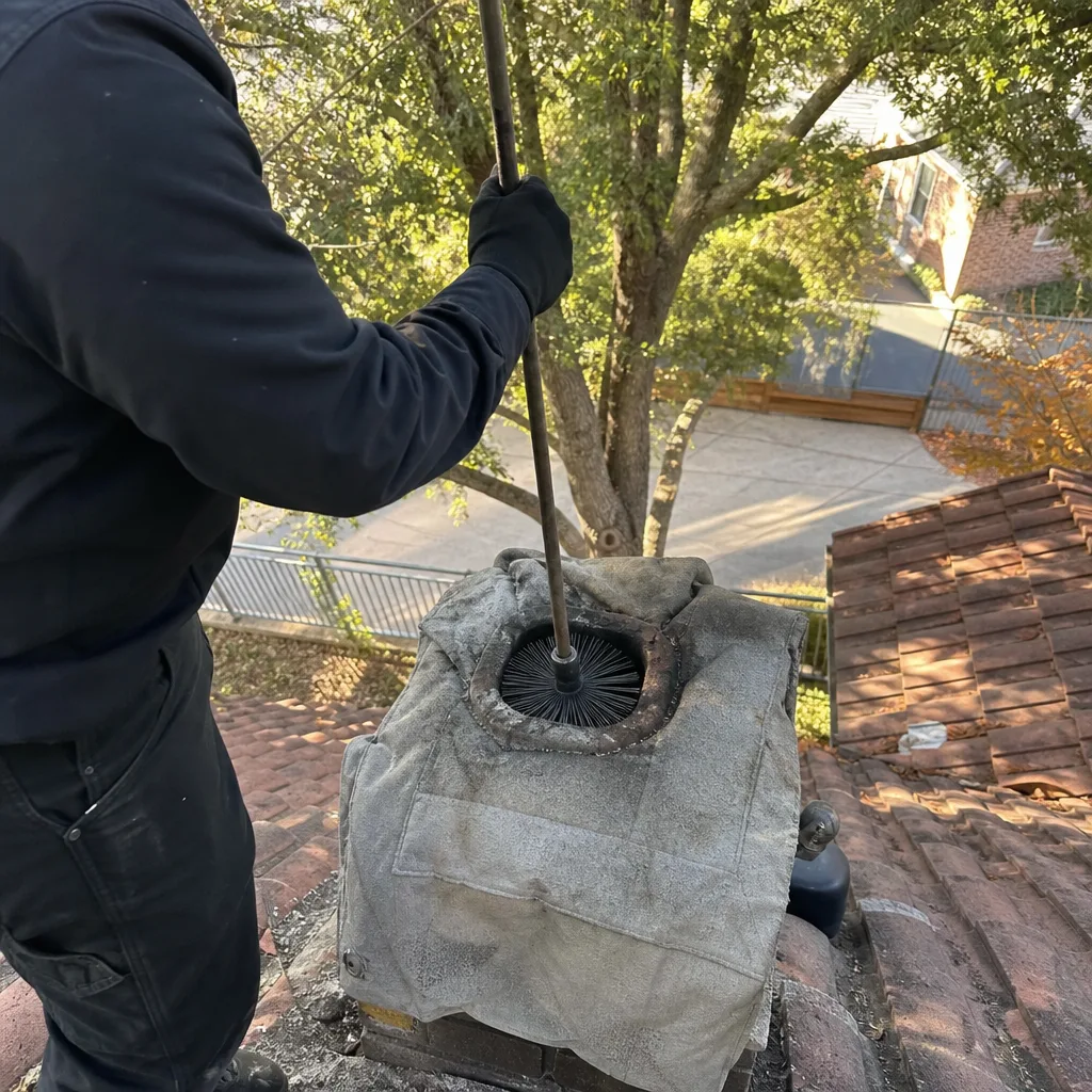 Professional chimney sweep cleaning a fireplace flue from the rooftop